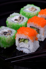 Fresh sushi rolls with cream cheese, rice, caviar and seafood against the black background. Asian cuisine meal