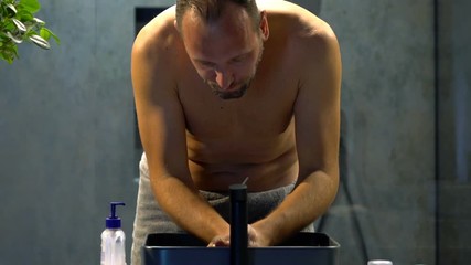 Young man washing face in bathroom