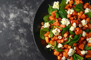 Healthy roasted sweet potato salad with spinach, feta cheese, hazelnut nuts in black plate