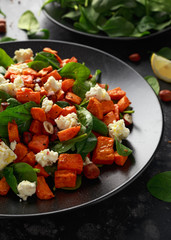 Healthy roasted sweet potato salad with spinach, feta cheese, hazelnut nuts in black plate