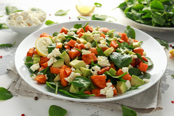 Avocado, roasted sweet potato, spinach, feta cheese healthy salad in white plate.