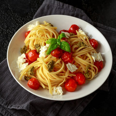 Pasta with green pesto sauce, roasted cherry tomatoes and mozzarella cheese in white plate on dark rustic background