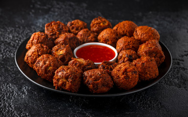 Indian Pakora snack spicy onion, red pepper with chilli sauce in a black plate