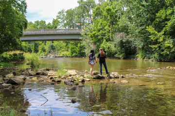 Couple holding hands walking across shallow stream on rocks