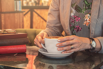 Young woman sit on coffee shop with cup of cappuccino, drinking aromatic,glasses with books, young woman spend weekend and tasting cappuccino.