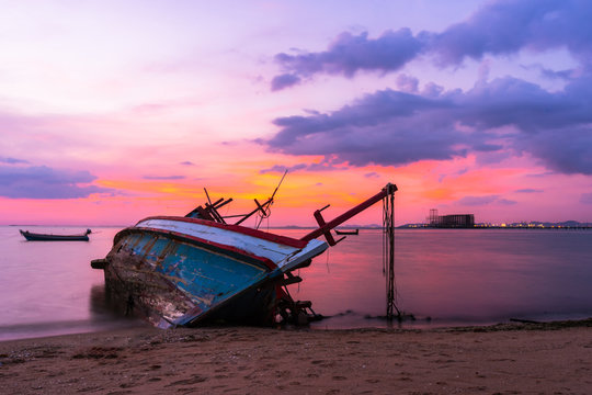Old fishing boat shipwrecks disposed on the beaches of the eastern coast of Thailand, view and landscape of the sea on sunset and sand with cloud sky.