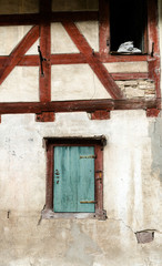 Fototapeta na wymiar Neunkirch, SH / Switzerland - November 10, 2018: historic half-timbered truss house with white walls and red wooden beams and a stone gargoyle statue leaning on the window still and staring out