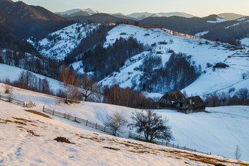 Spectacular winter landscape. Winter sunset, old rural mountain wooden chalets and snowy hills near Brasov, Transylvania, Romania, Europe