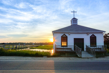 small white wooden chapel on the water on the coast during a colorful summer sunset with...