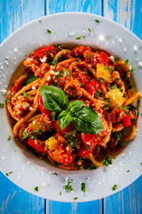 Pasta with meat, tomato sauce and vegetables on wooden table