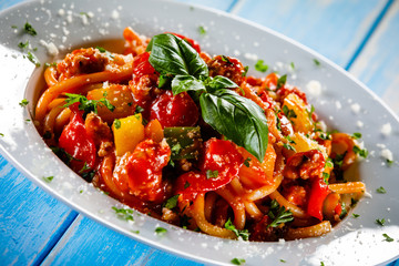Pasta with meat, tomato sauce and vegetables on wooden table