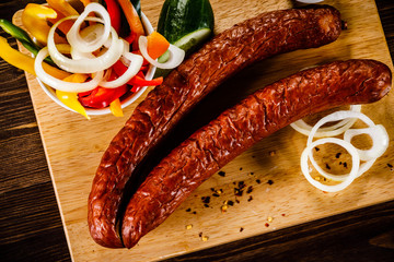 Raw sausages with vegetables on cutting board