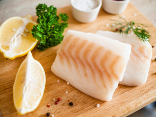 Fresh raw cod with herbs served on cutting board on wooden table