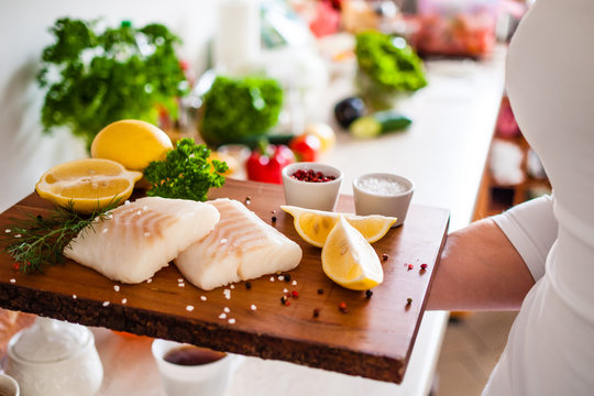 Fresh raw cod with herbs served on cutting board on wooden table
