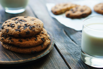 stack of homemade cookies with chocolate chips on baking paper and glass of fresh milk. 