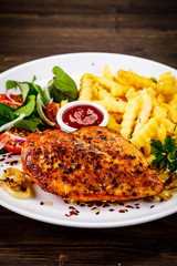 Grilled chicken fillet with french fries on wooden table