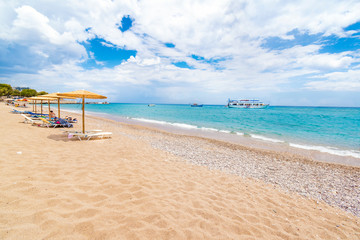 Stegna beach with sunshades, sunbeds and boats in background (RHODES, GREECE)