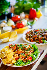 Grilled meat with nachos and vegetables on wooden background