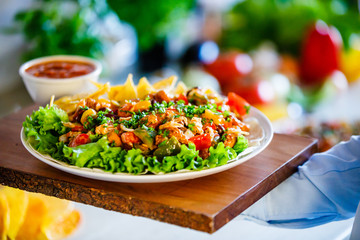 Grilled meat with nachos and vegetables on wooden background