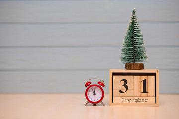 December 31st set on wooden calendar with new year tree and red alarm clock on blue background.