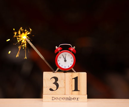 December 31st set on wooden calendar with red alarm clock on dark blurred background.