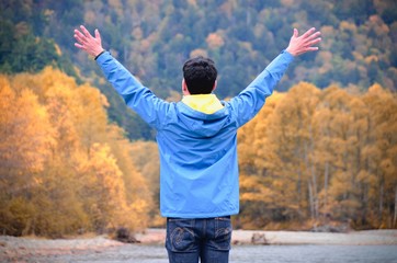 freedom man with hands up on the lake side against natural autumn forest and mountains