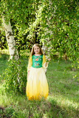 Blond young girl posing in a yellow green dress near birch trees