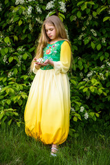Blond young girl posing in a yellow green dress near birch trees