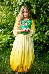 Blond young girl posing in a yellow green dress near birch trees
