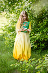 Blond young girl posing in a yellow green dress near birch trees