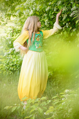 Blond young girl posing in a yellow green dress near birch trees