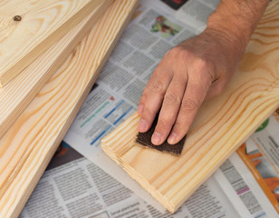 Man's hand with sandpaper polishes the board , wood treatment with sandpaper