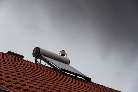 Solar water heater on rooftop, black storm clouds on the background, conceptual image of season ending for the heater.