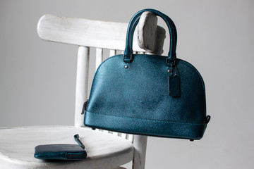 women leather bag and purse(dark green, blue, turquoise color) on a white wooden chair, advertising...