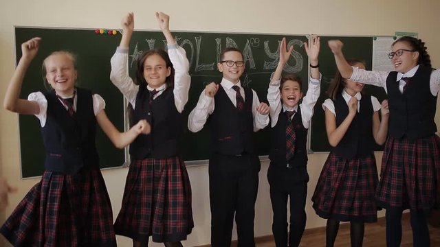 Happy students in school uniform having fun and jumping standing near the chalk board. College students celebrate the start of the holidays