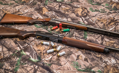 two shotguns of 16 and 12 gauge and cartridges on camouflage background
