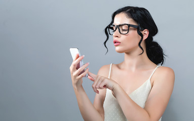 Young woman using her cellphone on a gray background