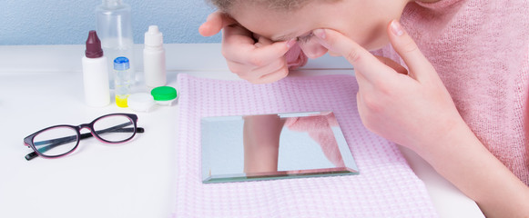girl sitting at the table, looking in the mirror and wearing contact lenses to improve vision