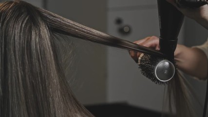 Close-up shot of woman having her hair drying and brushing in hair salon in slow motion.