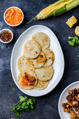COLOMBIAN FOOD. Maize AREPAS and fried pork chicharron ans colombian tomato sauce. Top view. Black background