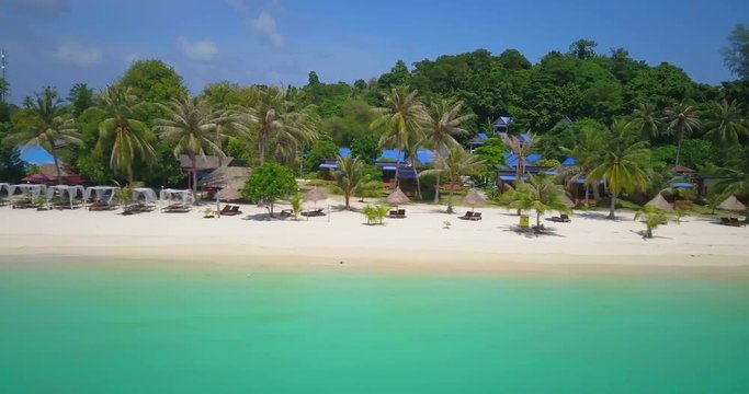 Sideways low elevation aerial drone view RL pan of beachfront resorts on white sand beach over emerald green sea on a beautiful sunny day on tropical Thai island, Ko Lipe, Thailand. 4k 1.9:1 23.976fps
