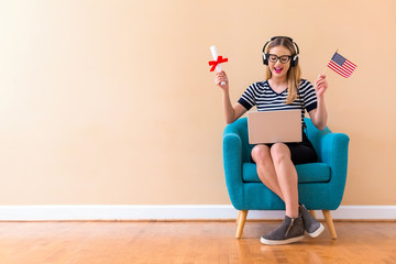 Young woman holding a diploma and USA flag with her laptop in a chair