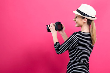 Young woman with a professional digital SLR camera on a pink background