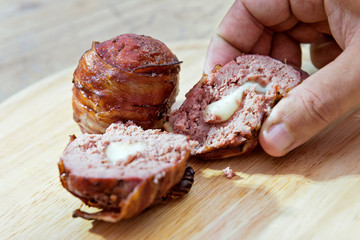 Meatballs stuffed with melted cheese and covered with bacon on cutting board