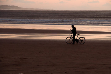 Fototapeta na wymiar Sunset on the beach with a man and his bicycle backlit