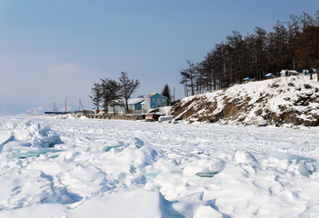 Lake Baikal in winter. Lonely blue wooden house near forest on shore. Russia