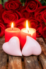 Obraz na płótnie Canvas Two red burning candles and pink hearts with fresh roses on wooden table