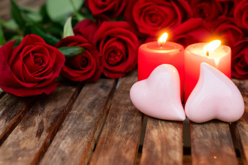Two red burning candles and pair of pink hearts with fresh roses on wooden table