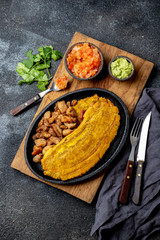 COLOMBIAN CARIBBEAN CENTRAL AMERICAN FOOD. Patacon or toston, fried and flattened whole green plantain banana on white plate with tomato sauce and chicharron Black background, top view