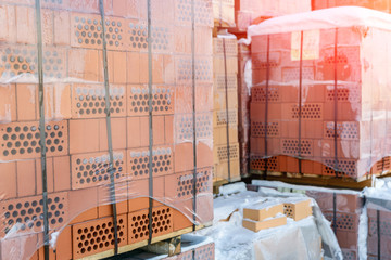Stock pallets of red bricks wrapped in stretch film at wholesale outdoor market ot store. Construction site with prepared materials